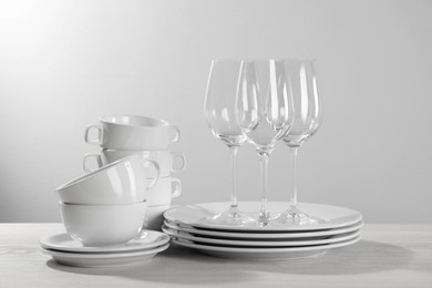 Photo of Set of clean dishware and glasses on white wooden table against light background