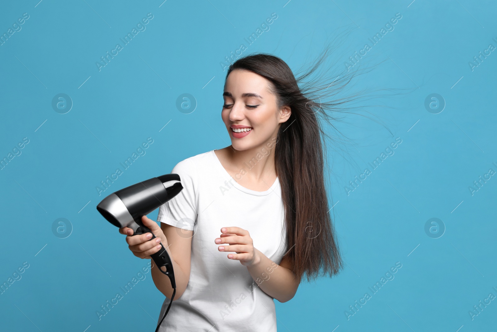 Photo of Beautiful young woman using hair dryer on light blue background