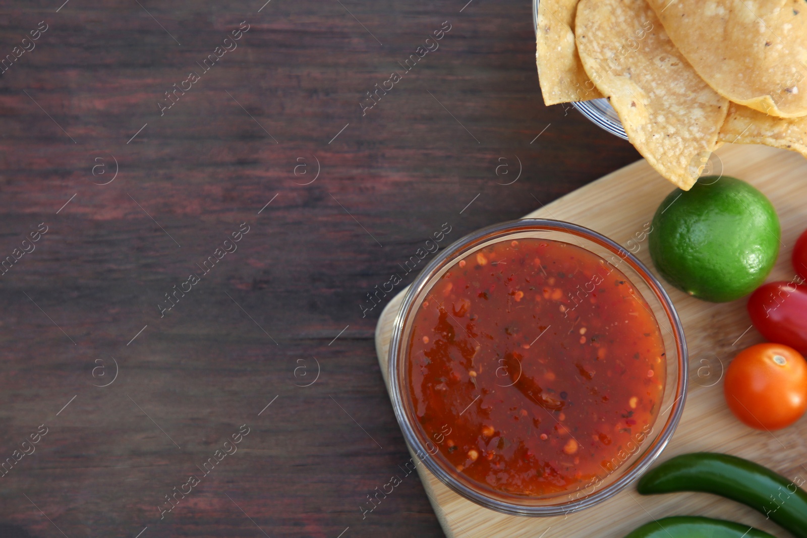 Photo of Tasty salsa sauce with tortilla chips and ingredients on wooden table, flat lay. Space for text