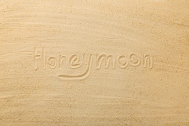 Word Honeymoon written on sand, top view