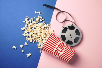 Tasty popcorn and film reel on color background, top view. Cinema snack