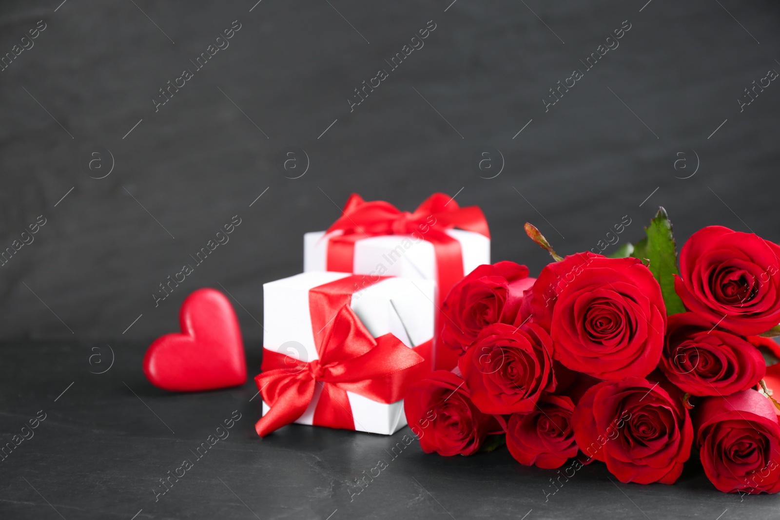 Photo of Beautiful red roses, gift boxes and decorative heart on dark table, space for text. St. Valentine's day celebration