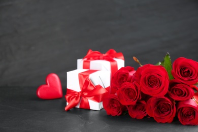 Photo of Beautiful red roses, gift boxes and decorative heart on dark table, space for text. St. Valentine's day celebration