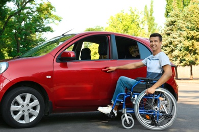 Photo of Young man in wheelchair opening door of car outdoors