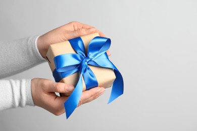 Photo of Woman holding gift box with blue bow on light grey background, closeup. Space for text