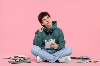 Portrait of student with notebook and stationery sitting on pink background