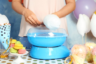 Photo of Woman making cotton candy using modern machine at table, closeup