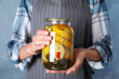 Photo of Woman holding jar with pickled zucchinis against blue background, closeup