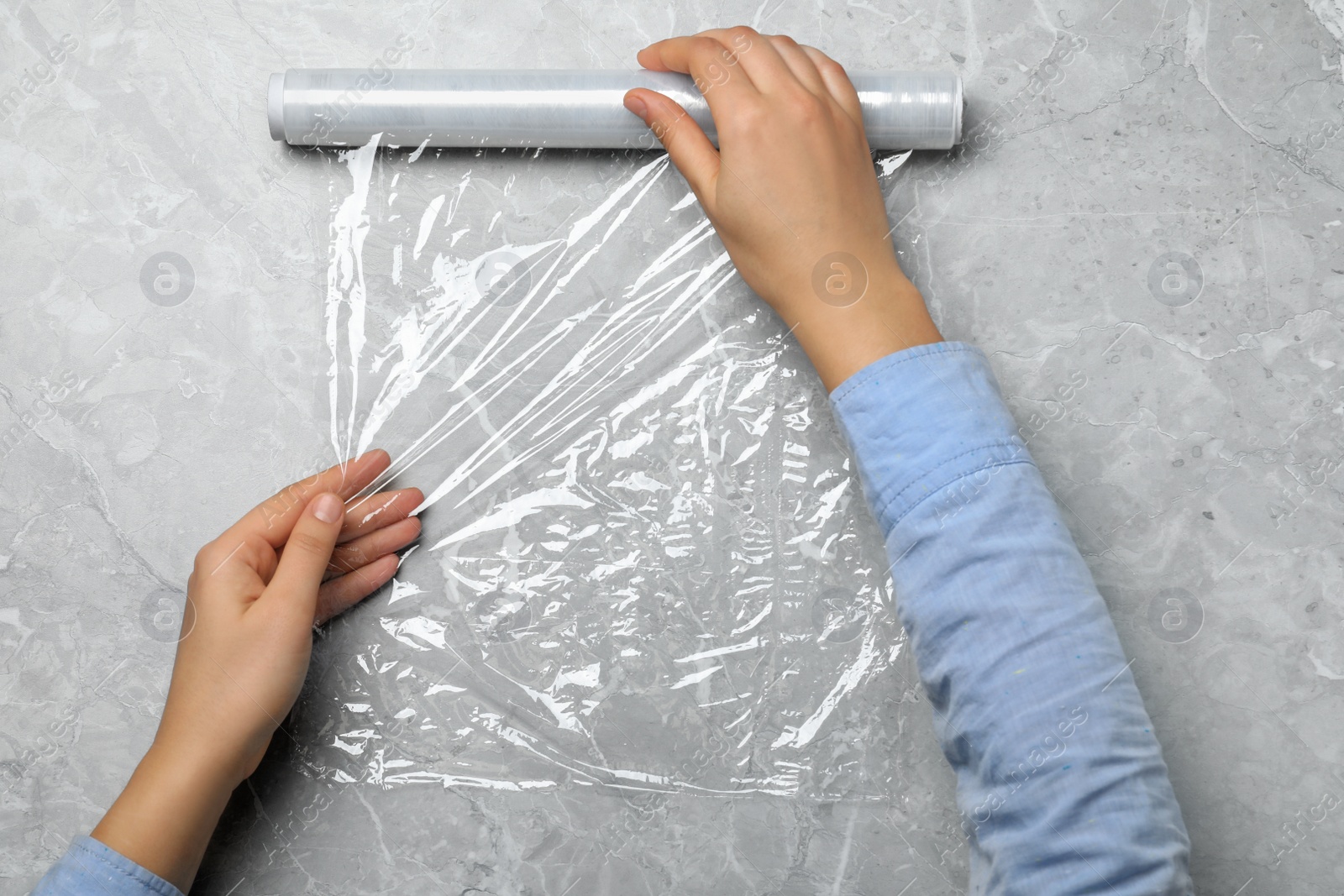 Photo of Woman with roll of stretch wrap at light grey table, top view