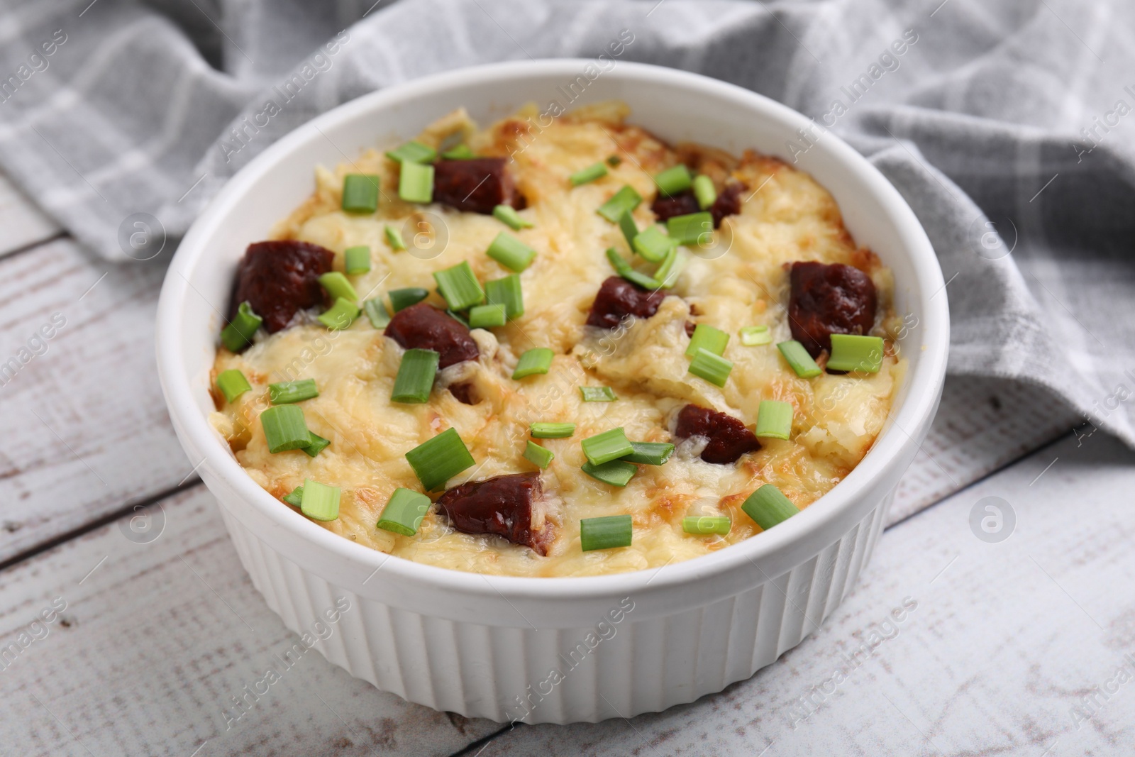 Photo of Tasty sausage casserole with green onion in baking dish on white wooden table, closeup