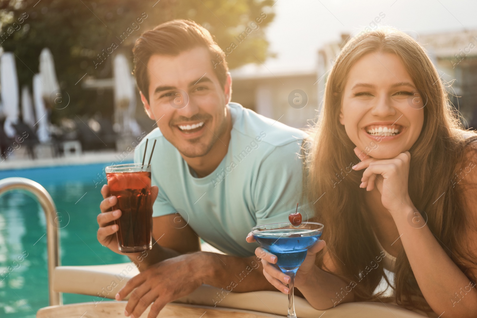 Photo of Happy young couple with fresh summer cocktails relaxing near swimming pool