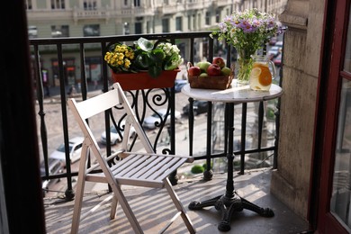 Photo of Relaxing atmosphere. Refreshing drink, apples and beautiful flowers on table near potted houseplants at balcony