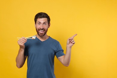 Photo of Emotional man holding sushi roll with chopsticks on orange background. Space for text