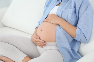 Photo of Beautiful pregnant woman sitting on sofa at home, closeup