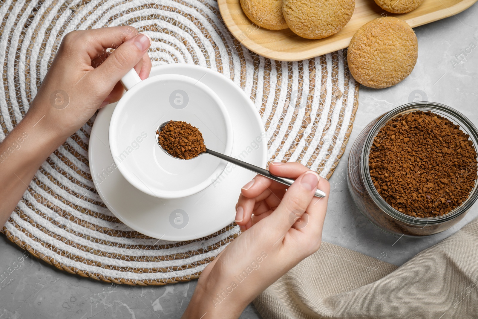 Photo of Woman pouring instant coffee into cup at light grey marble table, top view