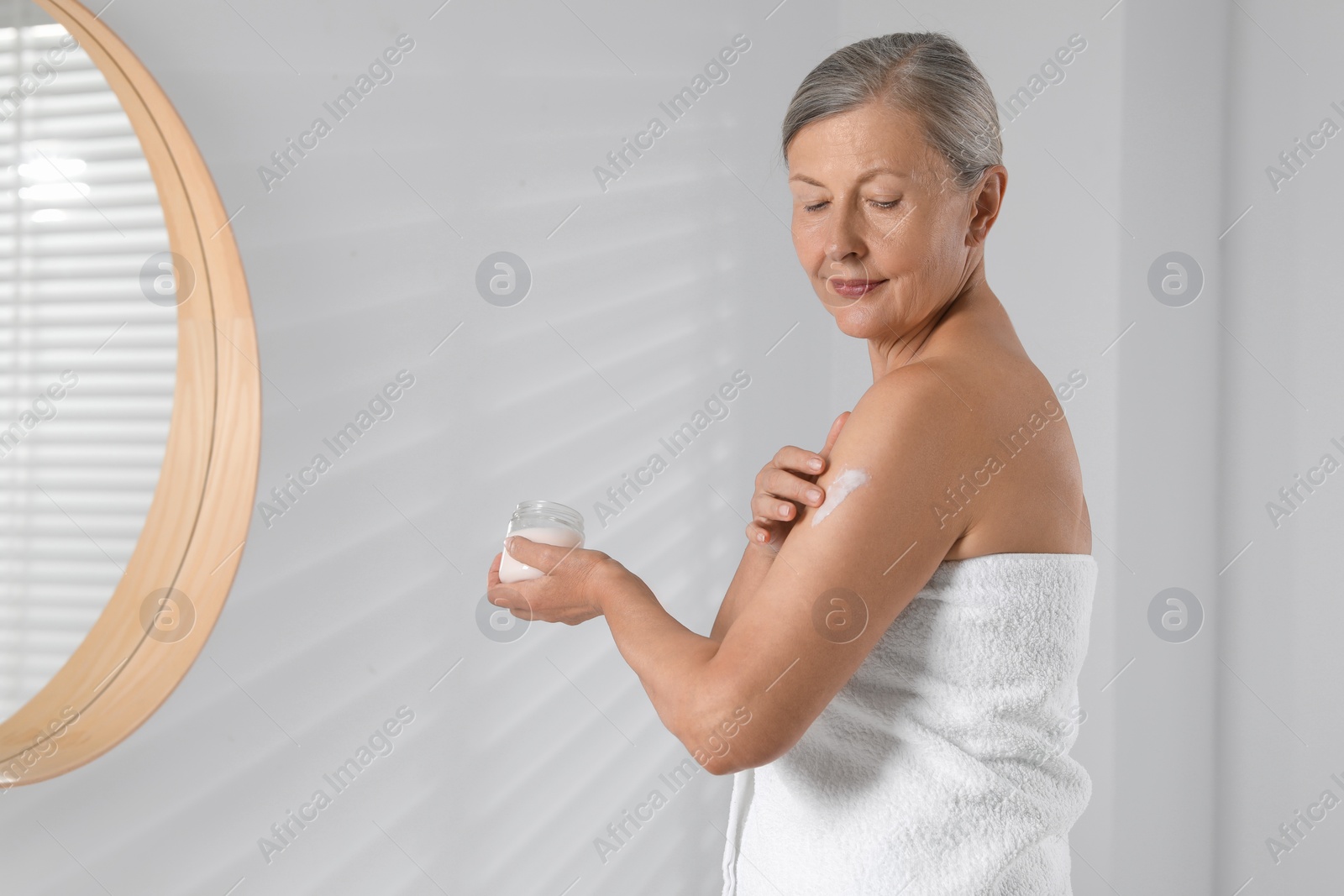 Photo of Happy woman applying body cream onto arm indoors. Space for text