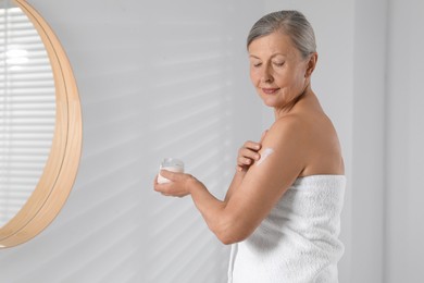 Happy woman applying body cream onto arm indoors. Space for text