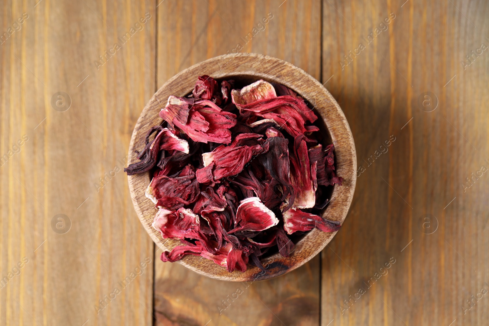 Photo of Dry hibiscus tea in bowl on wooden table, top view