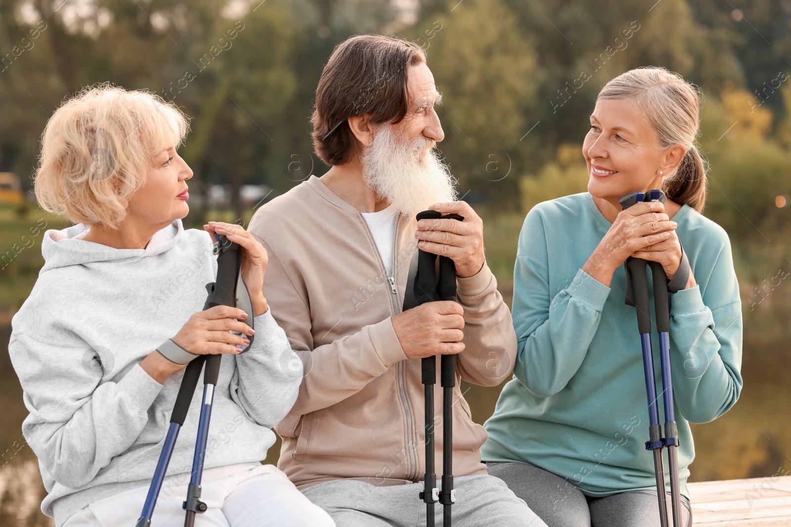 Photo of Group of senior people with Nordic walking poles sitting on wooden parapet outdoors