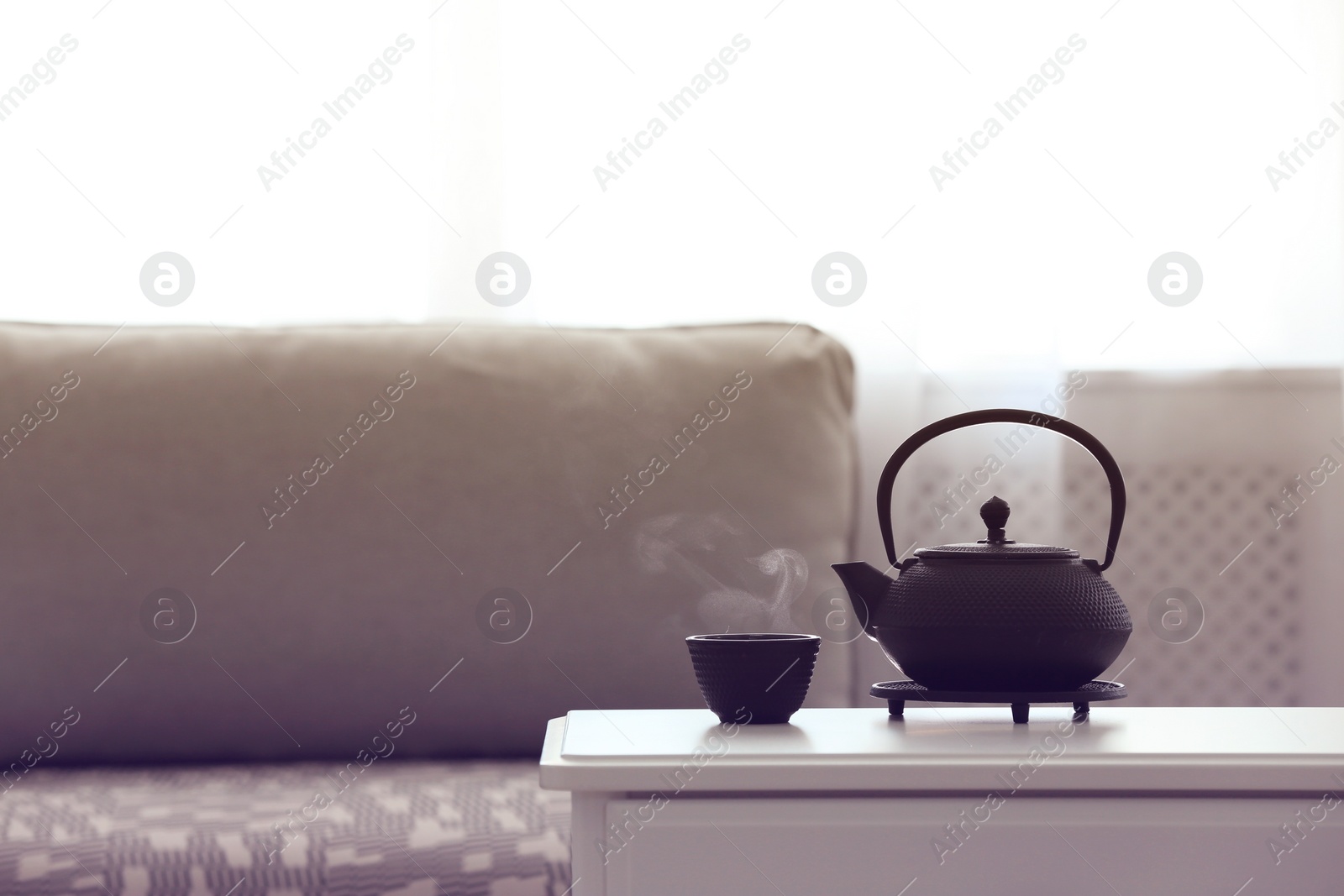 Photo of Teapot and cup of fresh hot tea on white table against blurred background. Space for text