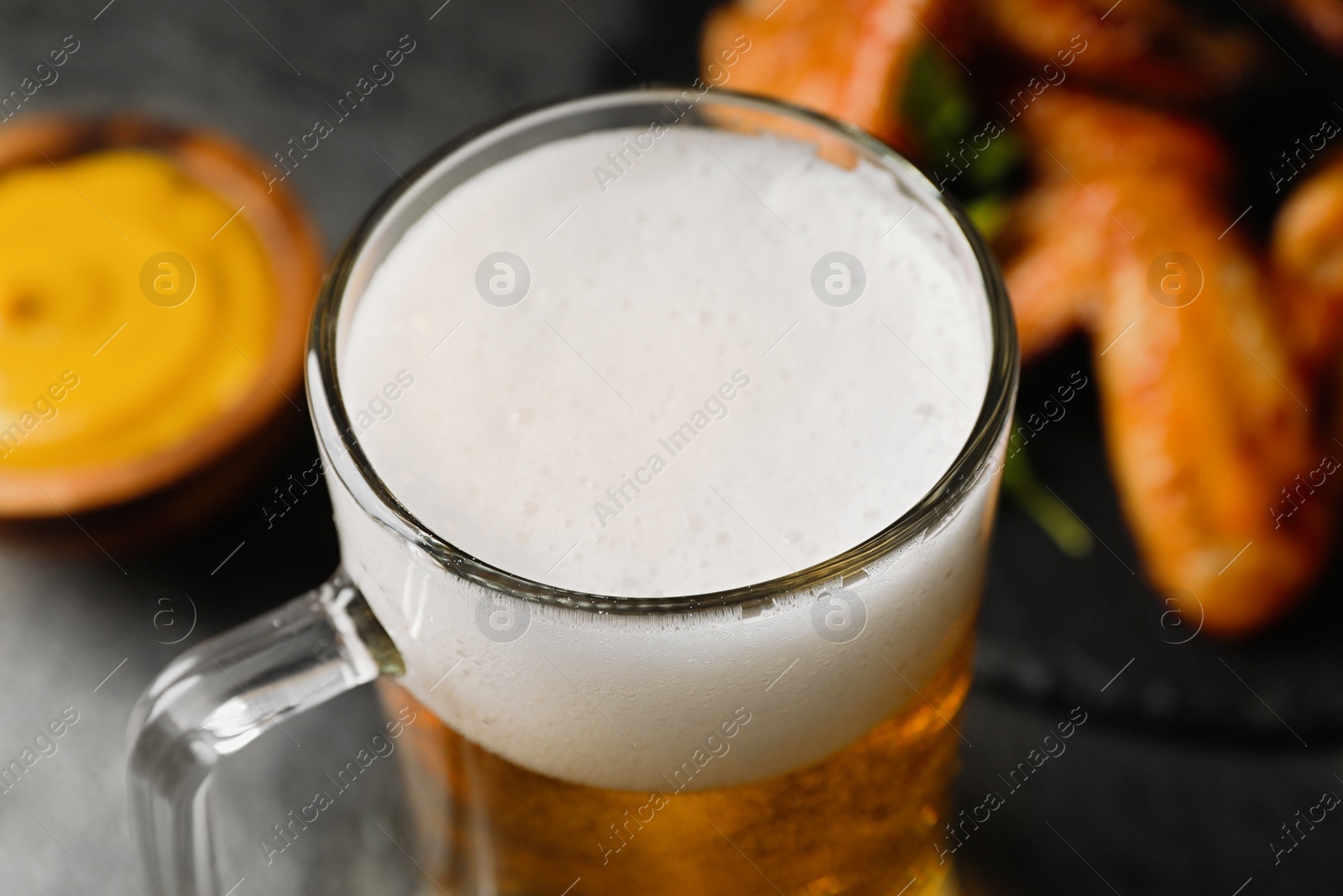 Photo of Mug with delicious beer and baked chicken wings on table, closeup