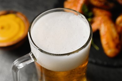 Mug with delicious beer and baked chicken wings on table, closeup