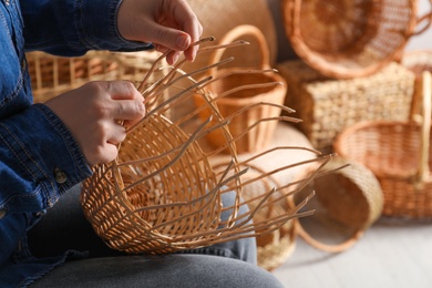 Photo of Woman weaving wicker basket indoors, closeup view