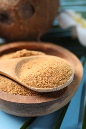 Photo of Coconut sugar in bowl, spoon and fruits on light blue wooden table, closeup