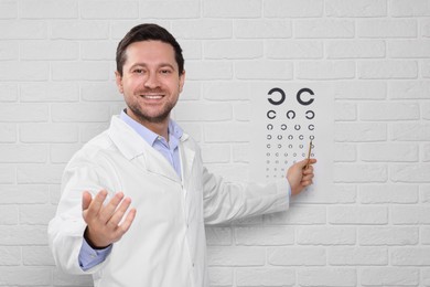 Photo of Ophthalmologist pointing at vision test chart on white brick wall