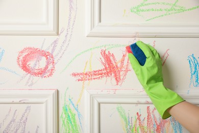 Photo of Woman erasing child's drawing from white wall, closeup