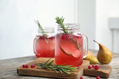 Photo of Tasty refreshing cranberry cocktail with rosemary in mason jars on table