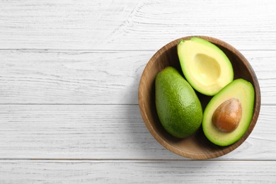 Photo of Bowl with ripe avocados on wooden background, top view