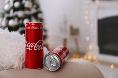 MYKOLAIV, UKRAINE - JANUARY 13, 2021: Cans of Cola-Cola in room with Christmas tree, space for text