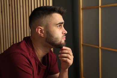 Photo of Sad young man at home. Space for text