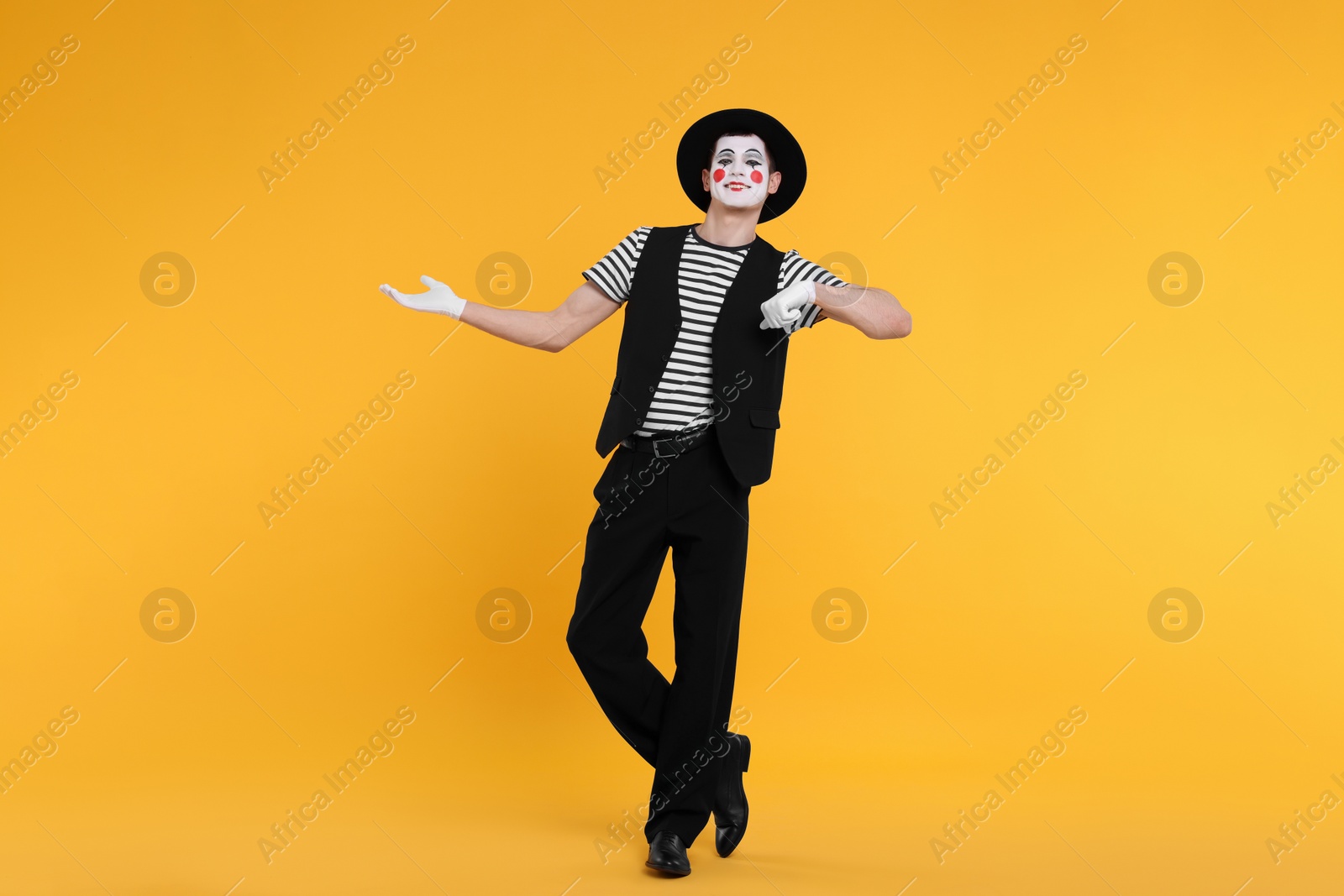 Photo of Funny mime artist in hat posing on orange background