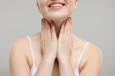 Smiling woman touching her neck on grey background, closeup