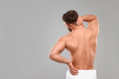 Photo of Man suffering from back and neck pain on grey background, back view. Space for text
