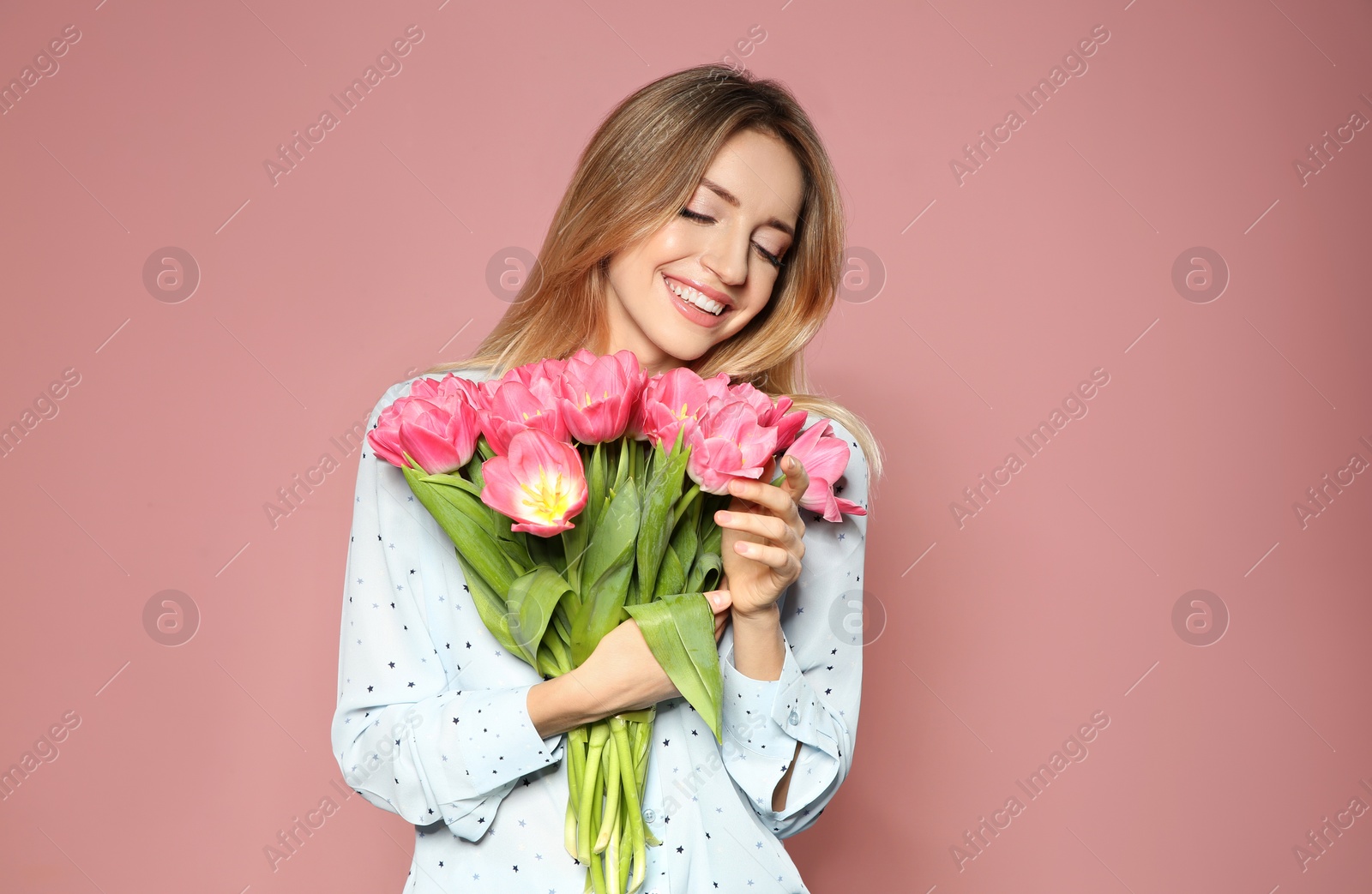 Photo of Portrait of beautiful smiling girl with spring tulips on pink background. International Women's Day