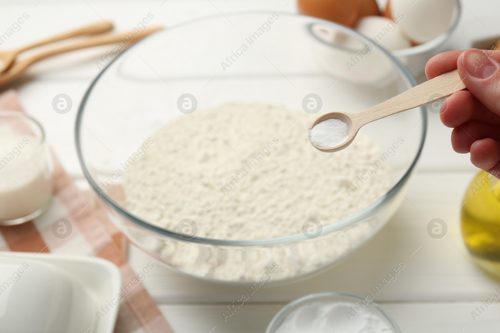 Photo of Woman taking spoon with baking powder from bowl at white table, closeup