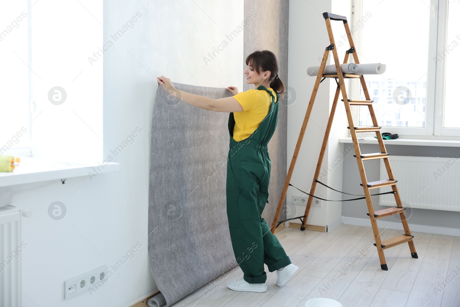 Photo of Woman hanging stylish gray wallpaper in room