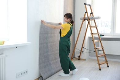 Photo of Woman hanging stylish gray wallpaper in room