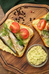 Photo of Delicious sandwiches with sprats, tomatoes, dill and avocado puree served on wooden table, top view