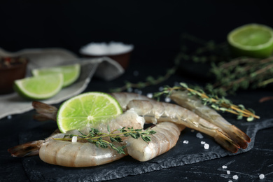 Photo of Fresh raw shrimps with lime and thyme on black table, closeup