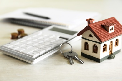 Calculator, house model, keys and documents on light table. Real estate agent's workplace