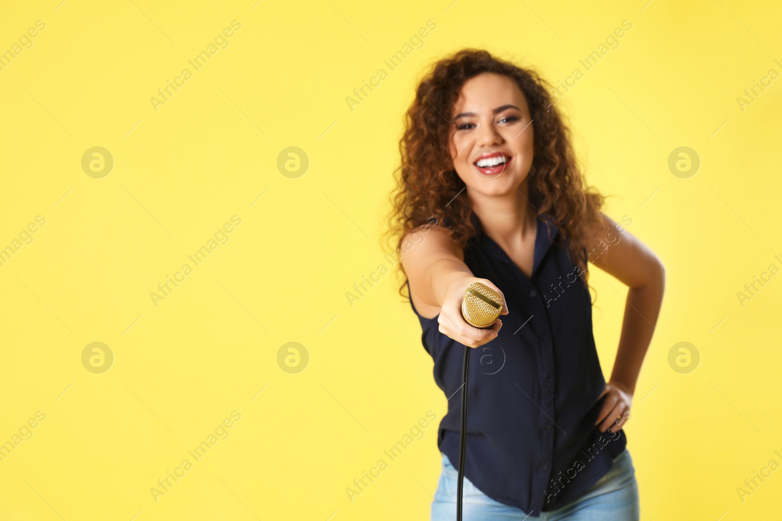 Photo of Curly African-American woman holding microphone on color background. Space for text