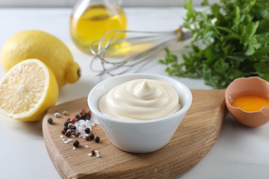 Photo of Tasty mayonnaise sauce in bowl, ingredients and spices on white table, closeup