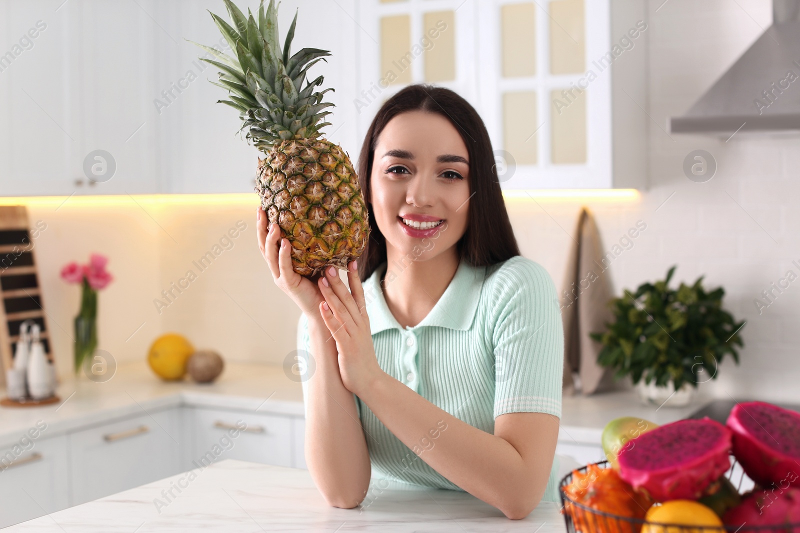 Photo of Young woman with fresh pineapple in kitchen. Exotic fruit