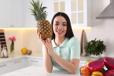 Photo of Young woman with fresh pineapple in kitchen. Exotic fruit