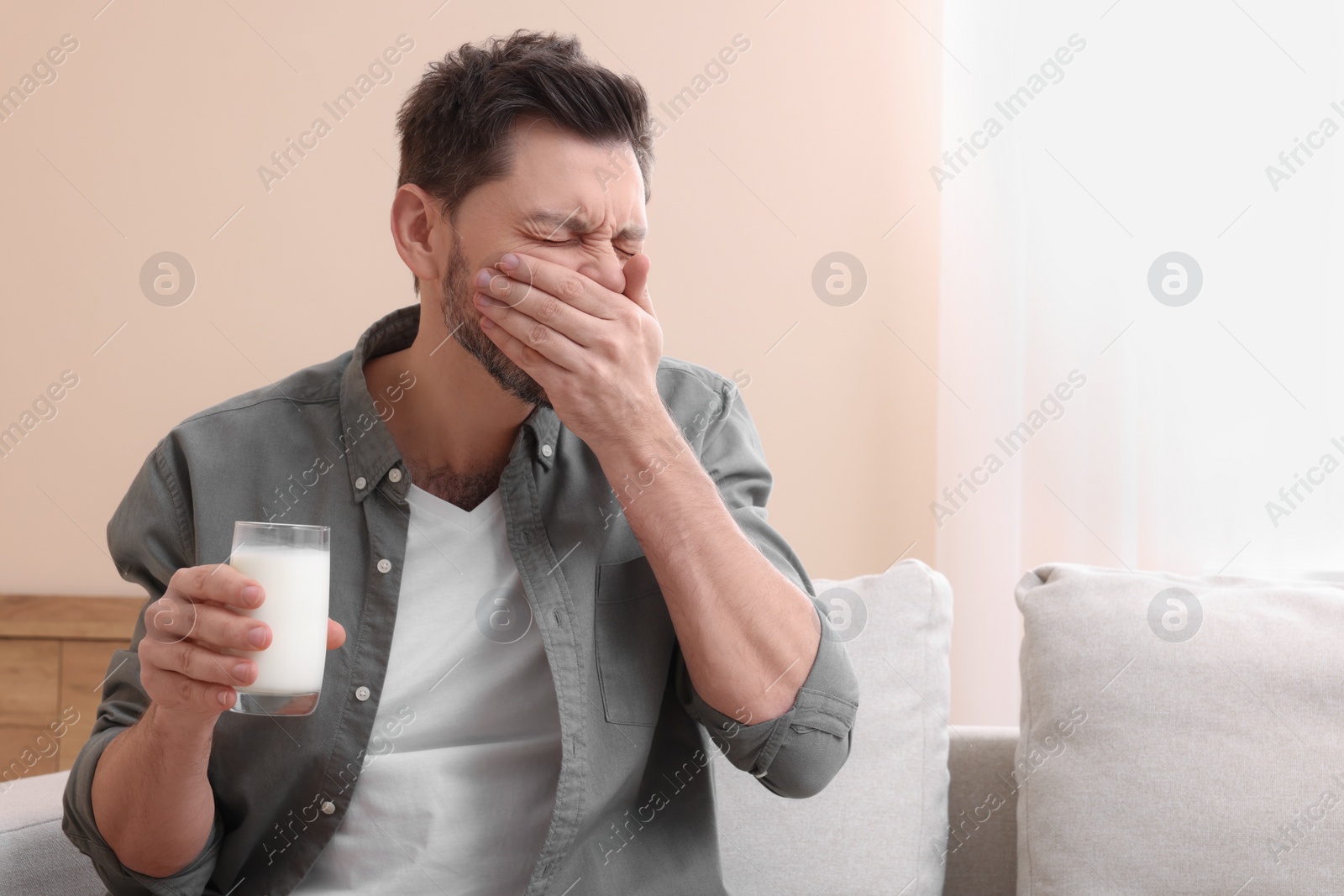Photo of Man with glass of milk suffering from lactose intolerance at home, space for text