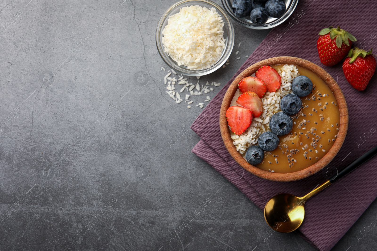 Photo of Delicious smoothie bowl with fresh berries, chia seeds and coconut flakes on grey table, flat lay. Space for text